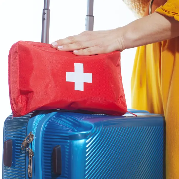 Hand resting on a red first-aid bag on top of blue luggage