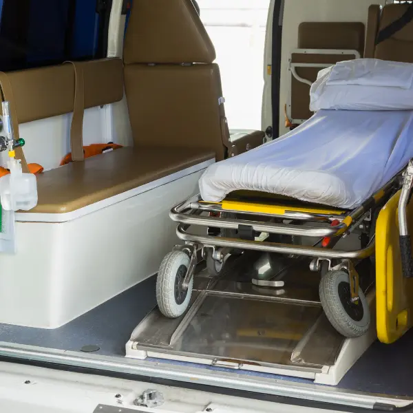 Medical transport stretcher with white bedding positioned on a vehicle loading platform
