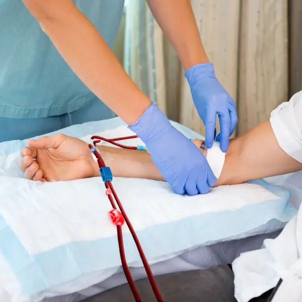 Medical professional wearing blue gloves caring for a patient's forearm beside dialysis tubing