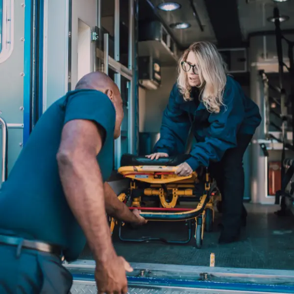 Two transport personnel positioning an empty stretcher at the rear of a medical transport vehicle