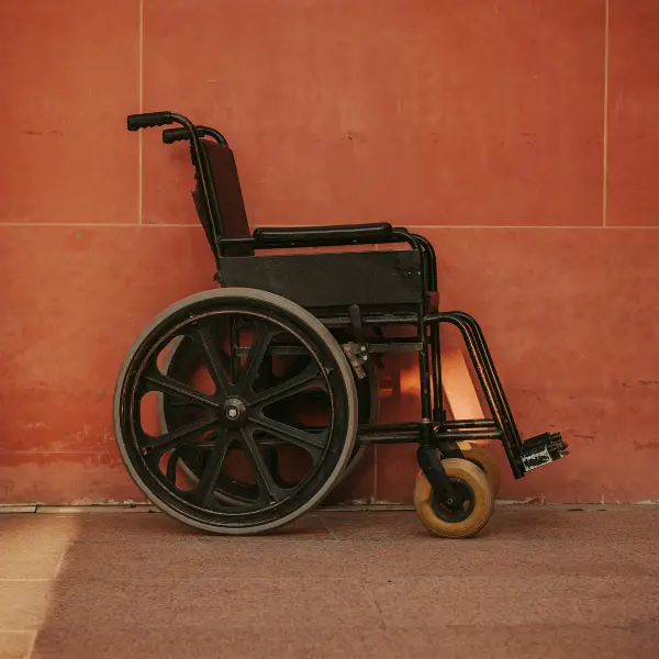 Side view of an empty black manual wheelchair against a terracotta-colored wall