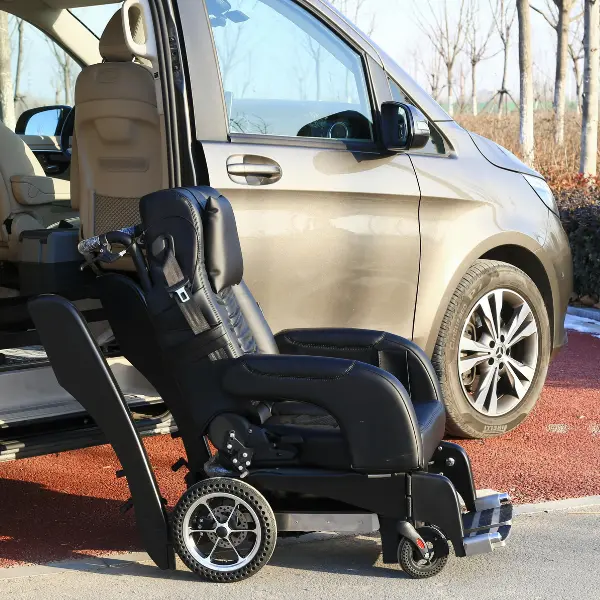 Black powered mobility chair positioned beside the open side door of a light-colored passenger vehicle