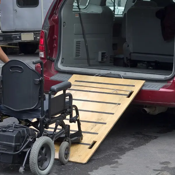 Manual wheelchair beside a fold-out access ramp extending from a red passenger van